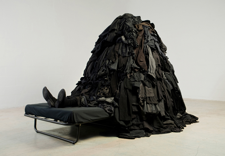 photo of a person in a cot under a pile of garments only boots showing