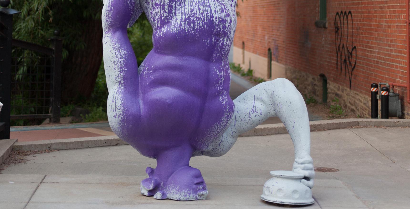an inverted statue of a man with abbreviated head painted purple outside