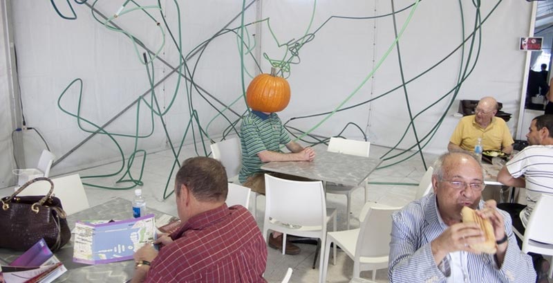 A man sitting in a cafeteria with a pumpkin on his head like you