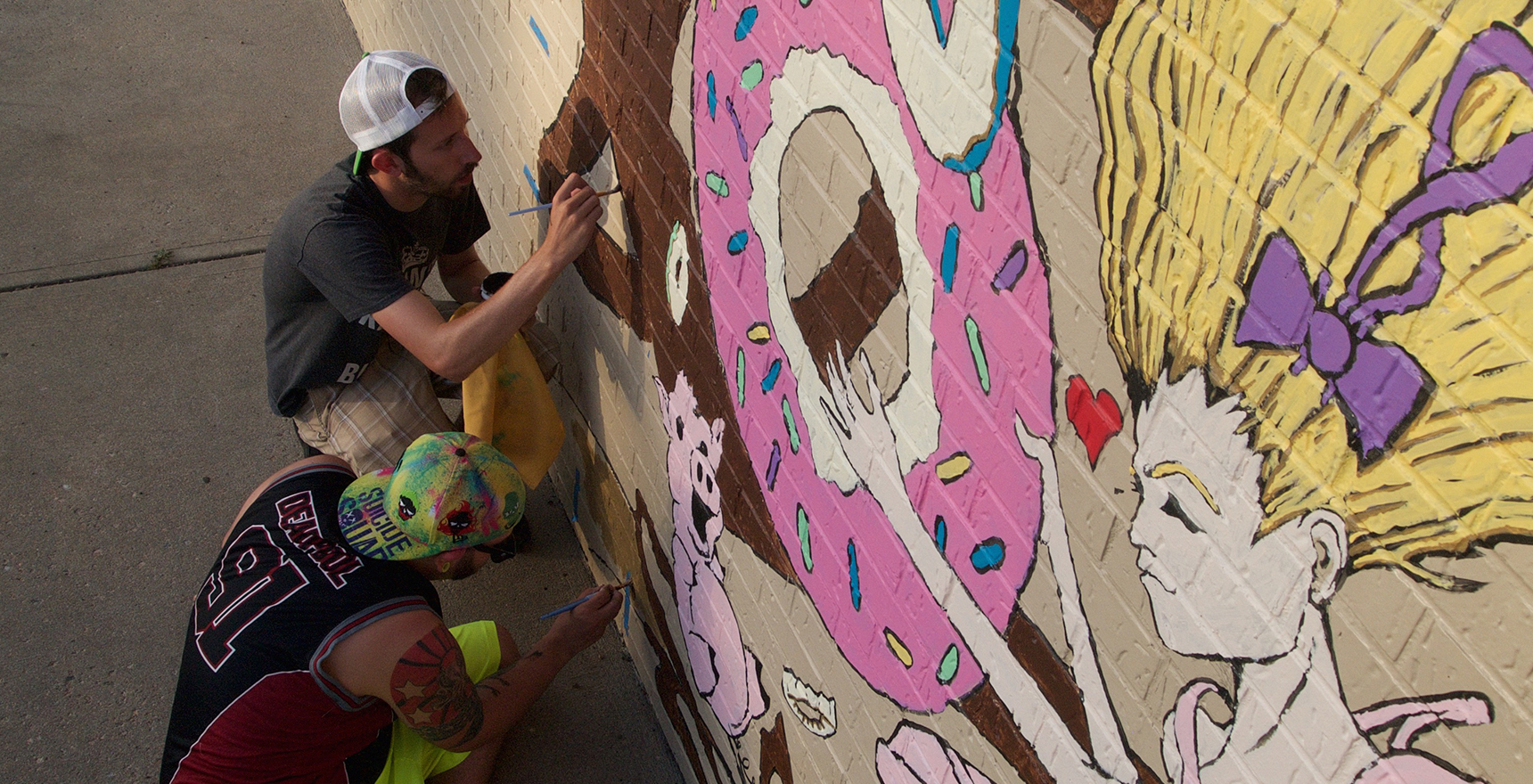 Aaron Van Dyke painting a mural featuring a girl holding a giant doughnut