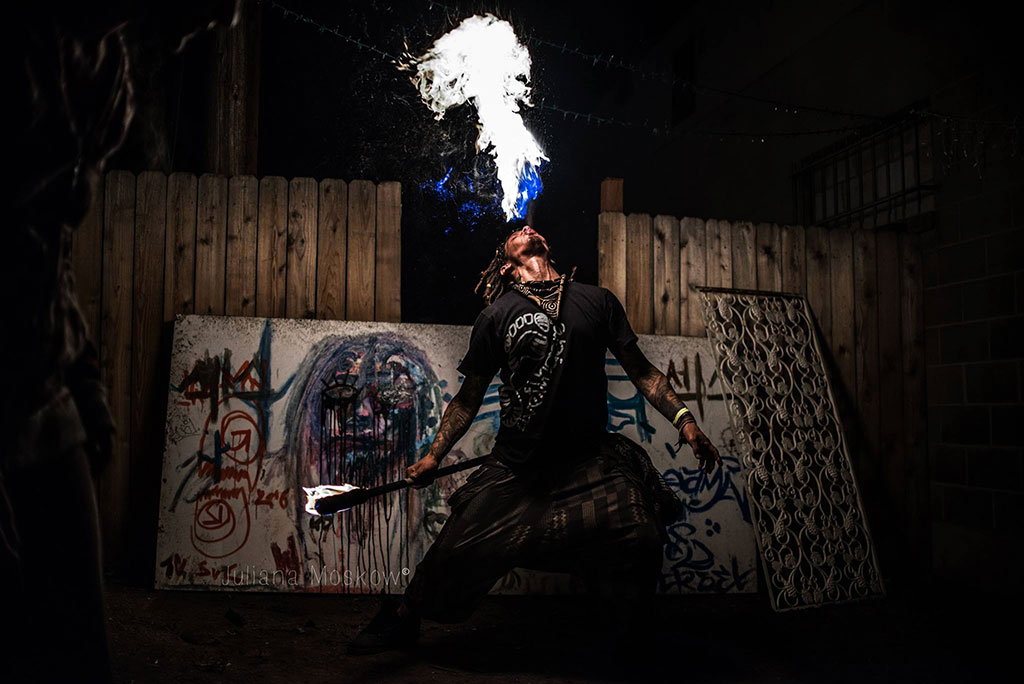 A man breathing fire in front of graffiti art