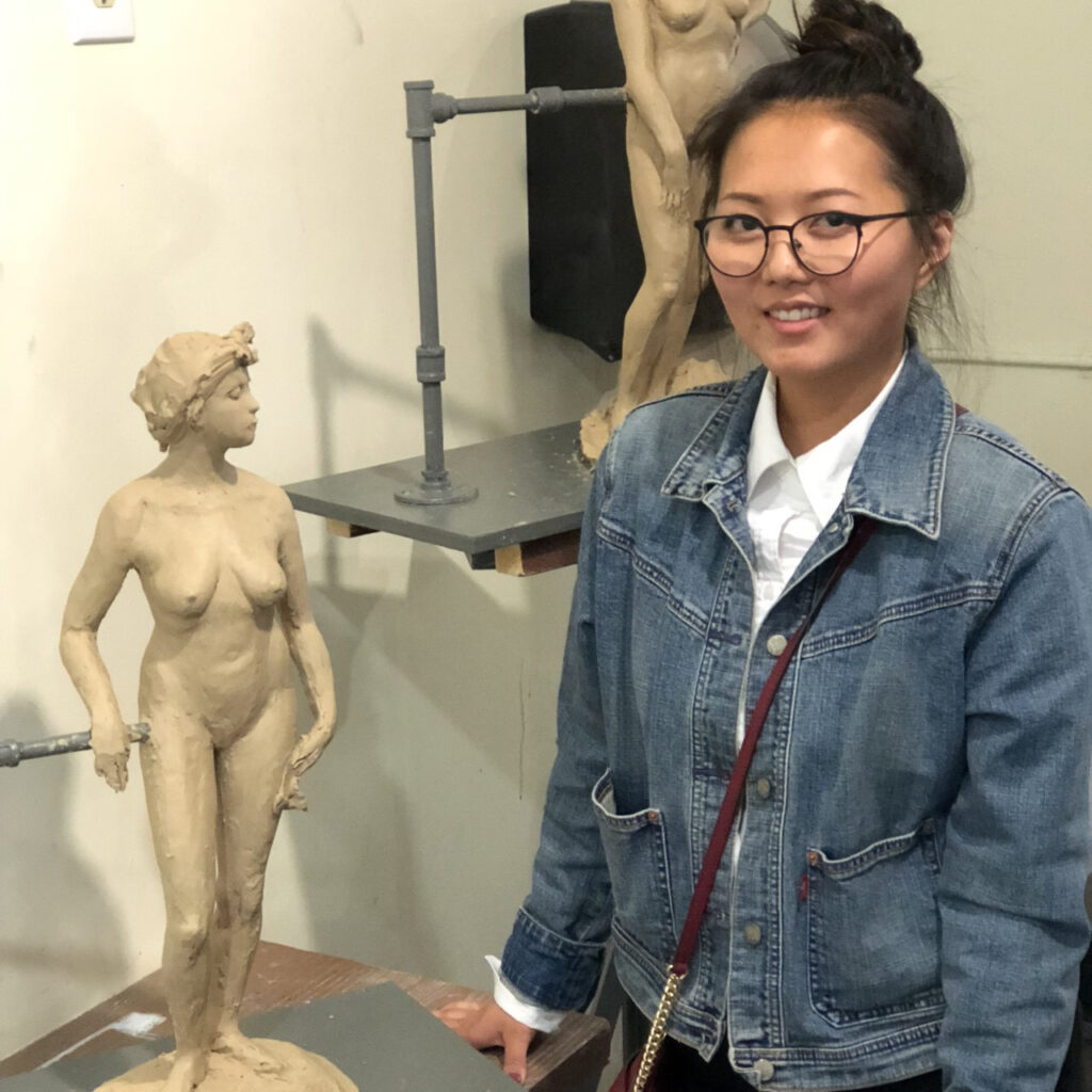 Photo of a sculptor standing next to a small clay nude